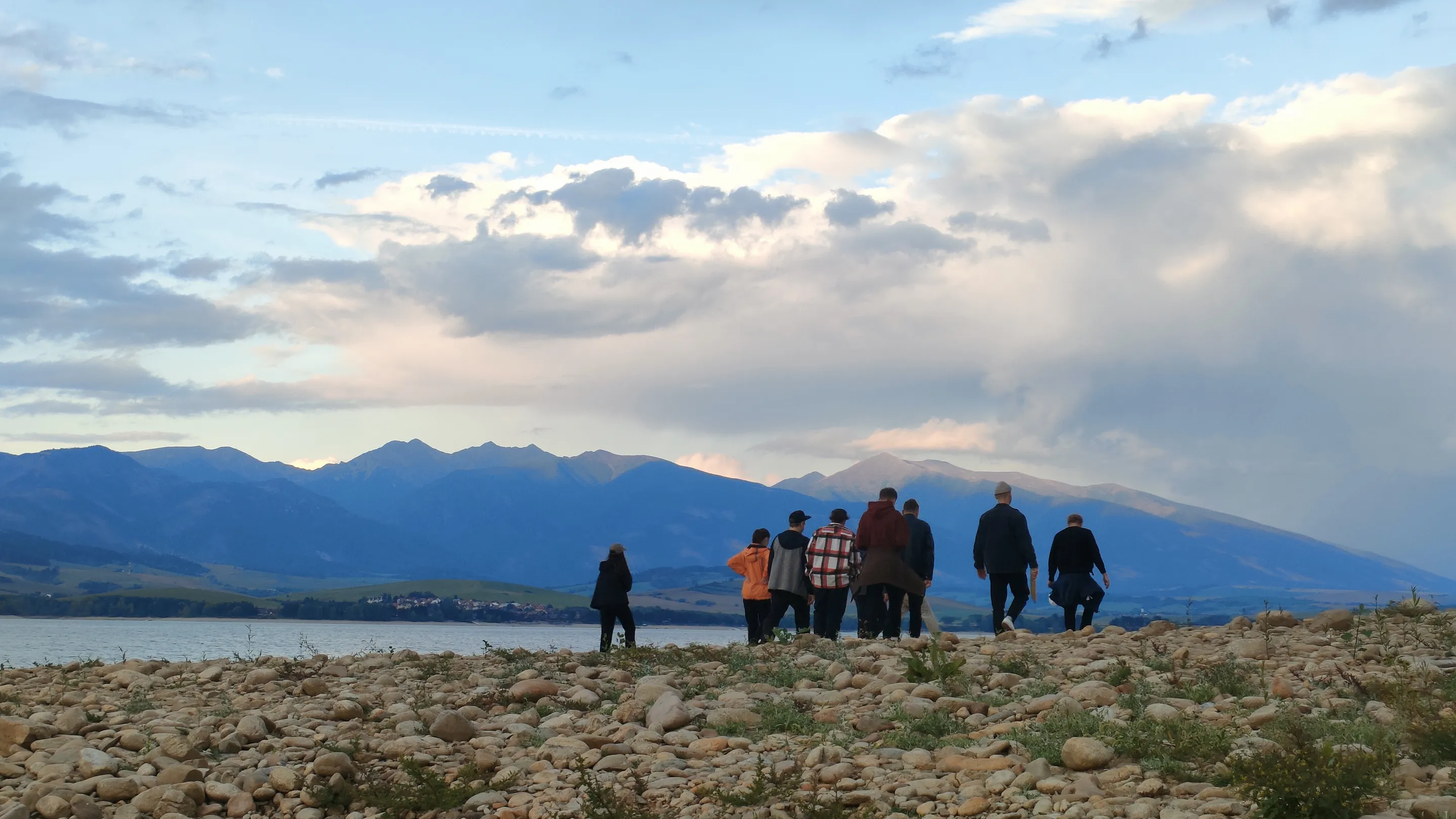 Order Group team members standing on a rocky lakeshore with mountains at sunset