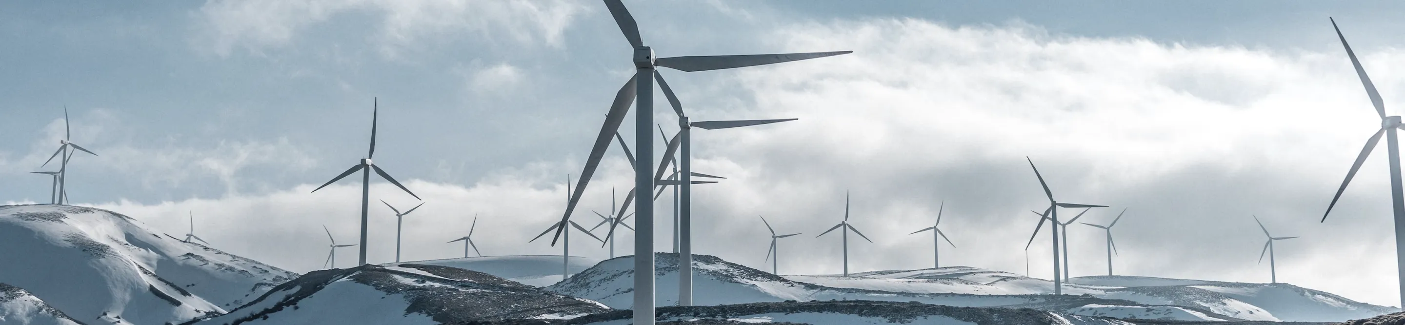 Wind turbines on snowy hills under a cloudy sky